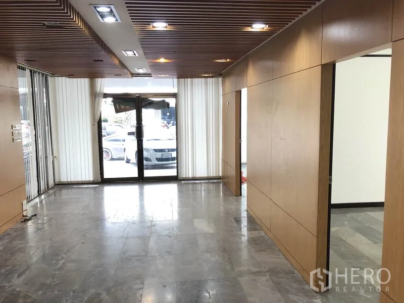 Home Office for rent in Huai Khwang, Bangkok - Ground-floor lobby with wood wall panels, marble flooring, recessed ceiling lights and a glass entrance.