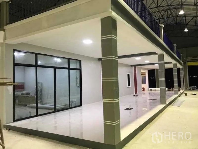 Warehouse for rent in Bang Pakong, Chachoengsao - Ground-floor office area with sliding glass doors beneath a mezzanine and bright column lighting.