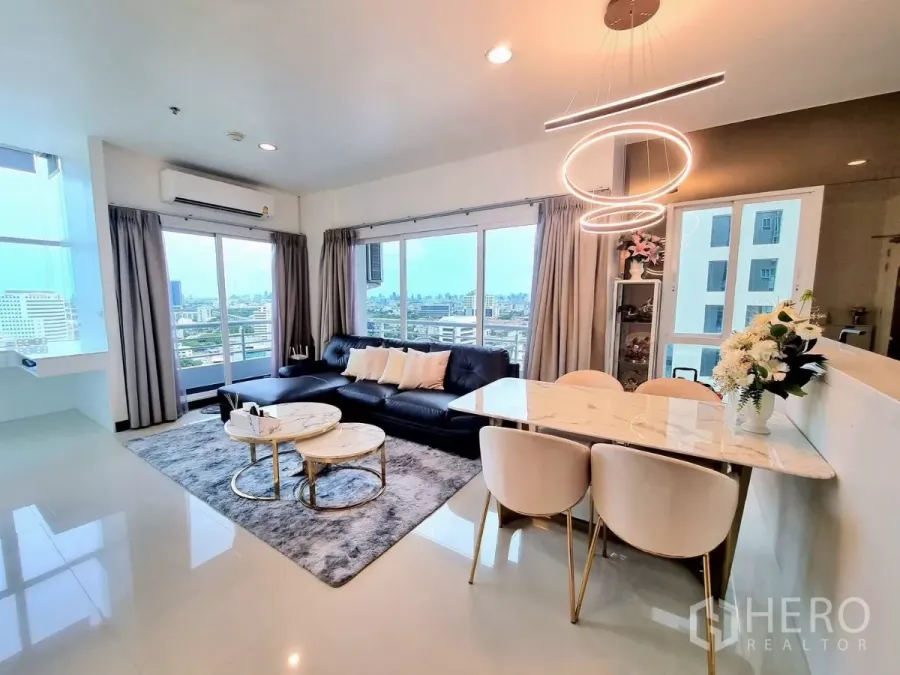 Condominium for rent in Bang Kapi, Bangkok - Bright living and dining area with black sofa, marble tables, and large windows overlooking the Bangkok skyline.