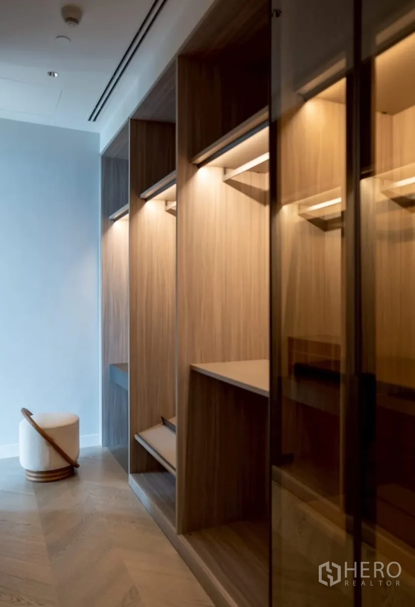Condominium for rent or sale in Pathum Wan, Bangkok - Walk-in closet with illuminated wooden shelving and glass-front cabinetry.