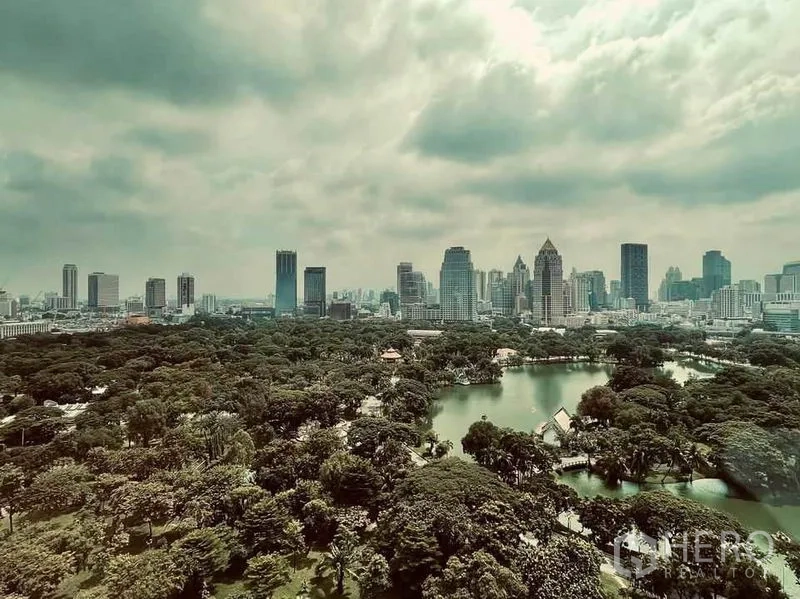 Condominium for sale in Pathum Wan, Bangkok - Aerial view of Lumpini Park lake and Bangkok city skyline under dramatic clouds.