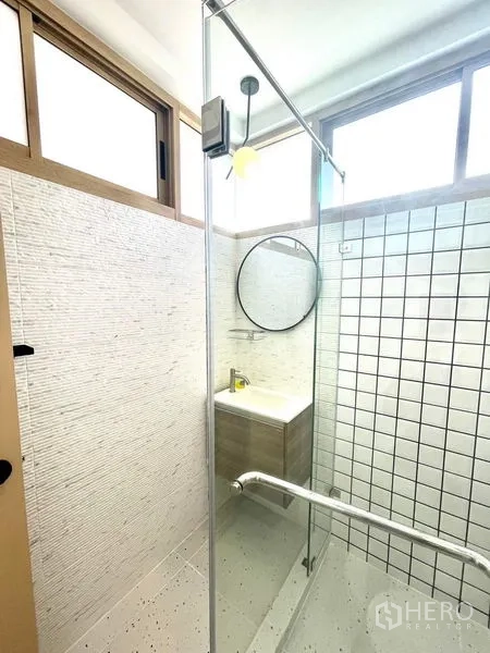 Townhouse for rent in Khlong Toei, Bangkok - Compact bathroom with glass shower, round mirror and window lighting.
