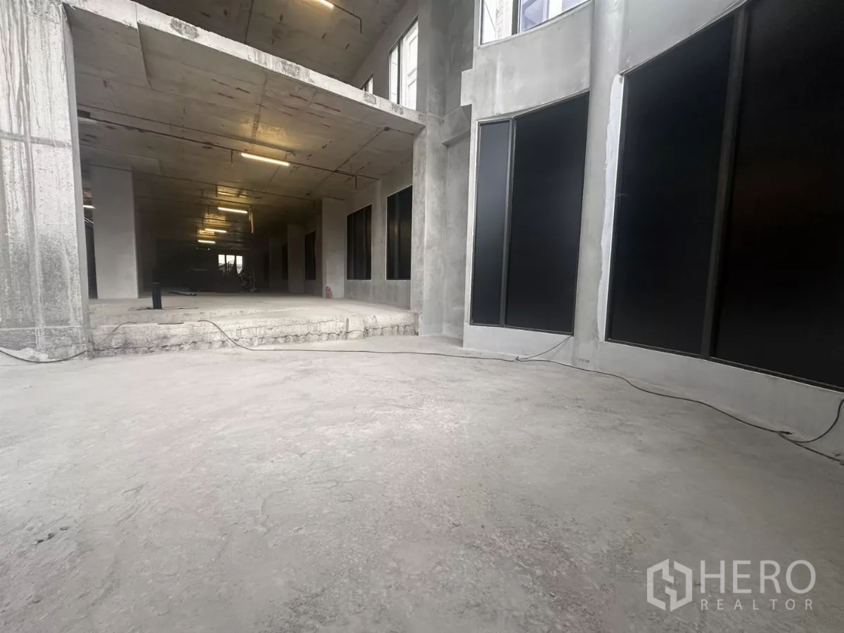 Retail Space for rent in Watthana, Bangkok - Open-plan ground floor retail area with unfinished concrete and sweeping glass facade.