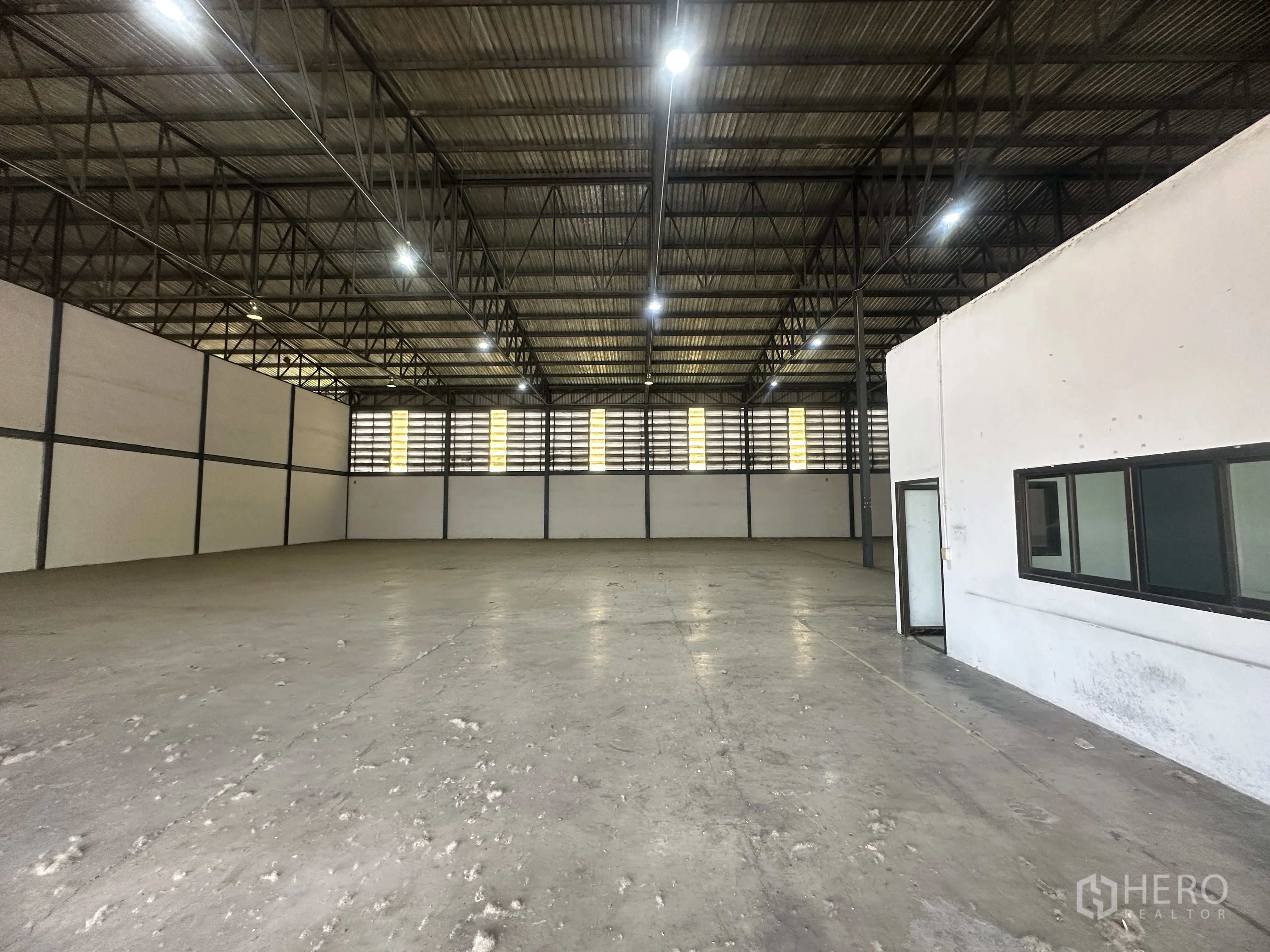 Warehouse for rent in Khlong Luang, Pathum Thani - View of the warehouse floor beside the internal office with windows and door.