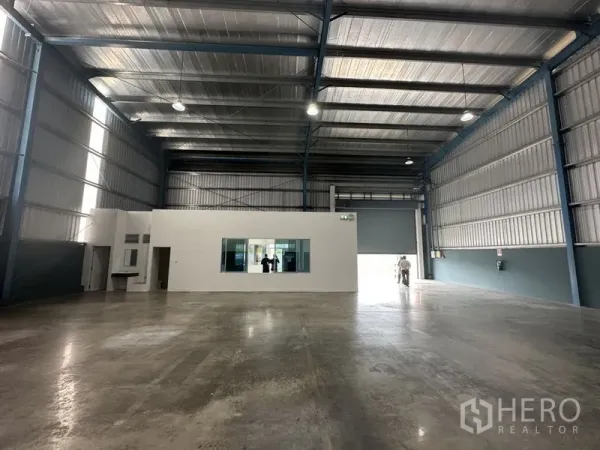 Factory for rent in Bang Phli, Samut Prakan - Open warehouse bay featuring a central white office block, bright LED lighting and a large roller shutter door.