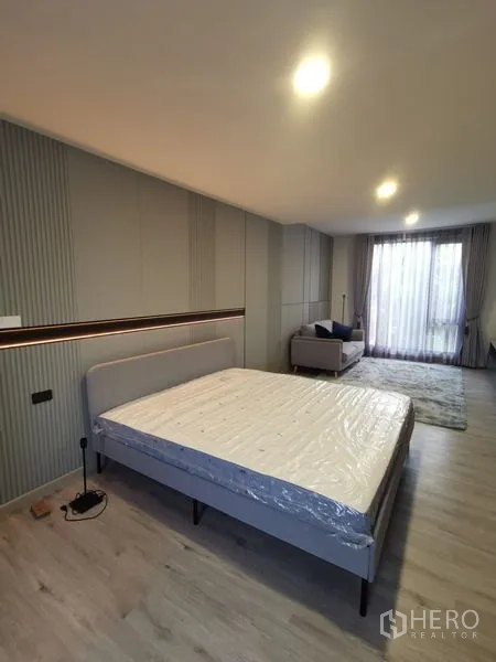 Townhouse for rent in Bang Phli, Samut Prakan - Large bedroom with wall panels, balcony-facing window, sofa nook and warm lighting.