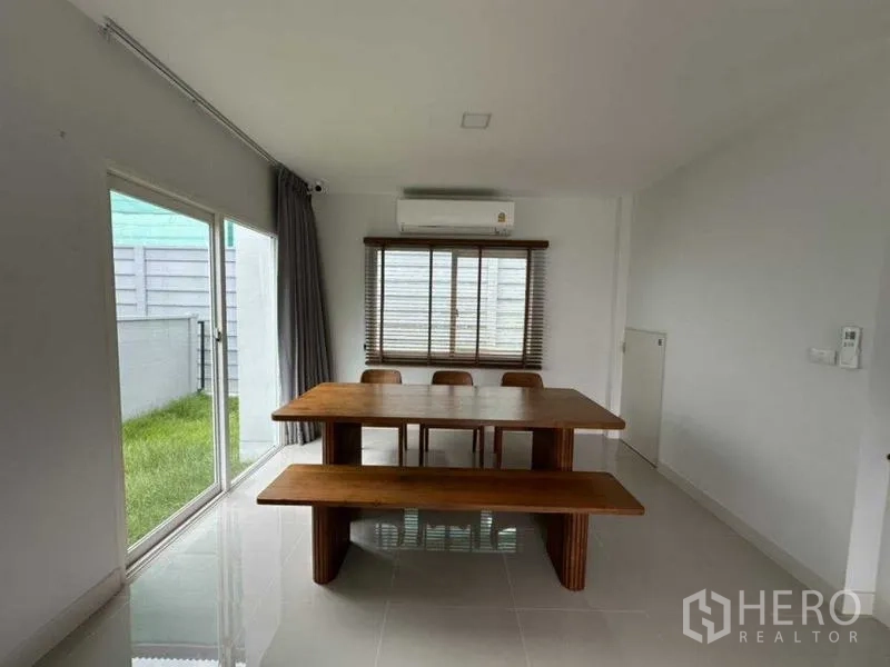 Townhouse for rent in Bang Phli, Samut Prakan - Dining area with solid wood table and bench beside sliding doors and a small lawn.