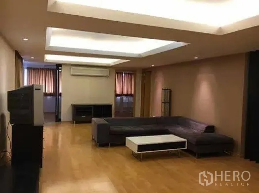 Condominium for rent in Watthana, Bangkok - Spacious living room with L-shaped sofa, recessed ceiling lights, wood flooring, and a media console.
