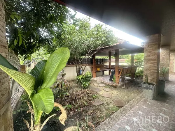 Detached House for sale in Pathum Thani - Shaded outdoor pavilion with bench seating surrounded by mature trees in the front garden.