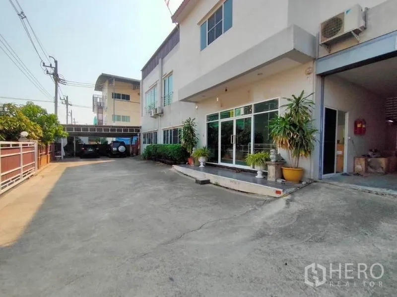 Warehouse for sale in Mueang Samut Sakhon, Samut Sakhon - Glass-front office entrance and roller-shutter loading bay along the concrete driveway.