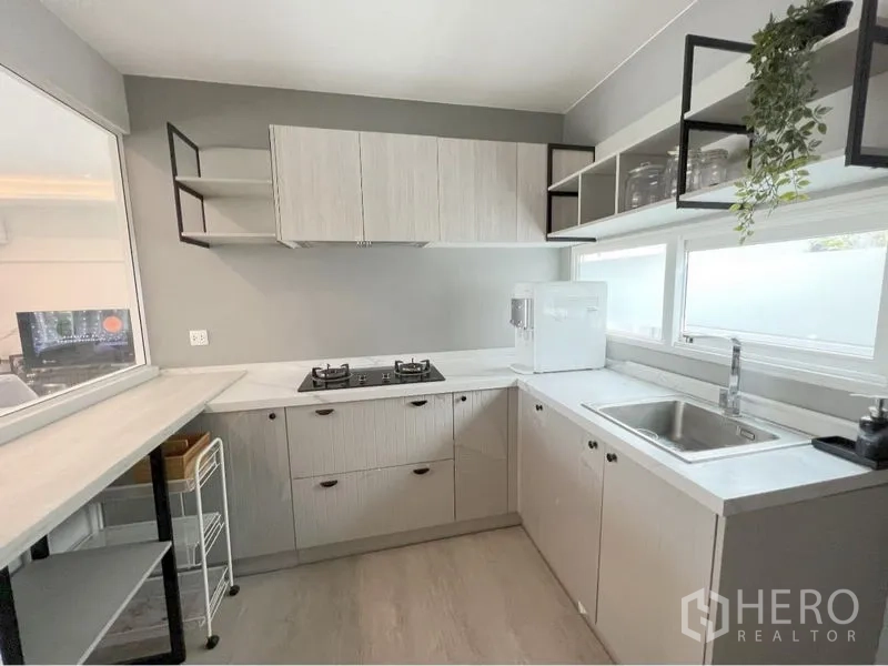 Detached House for rent or sale in Prawet, Bangkok - Modern U-shaped kitchen with gas hob, sink and wide windows for natural light.