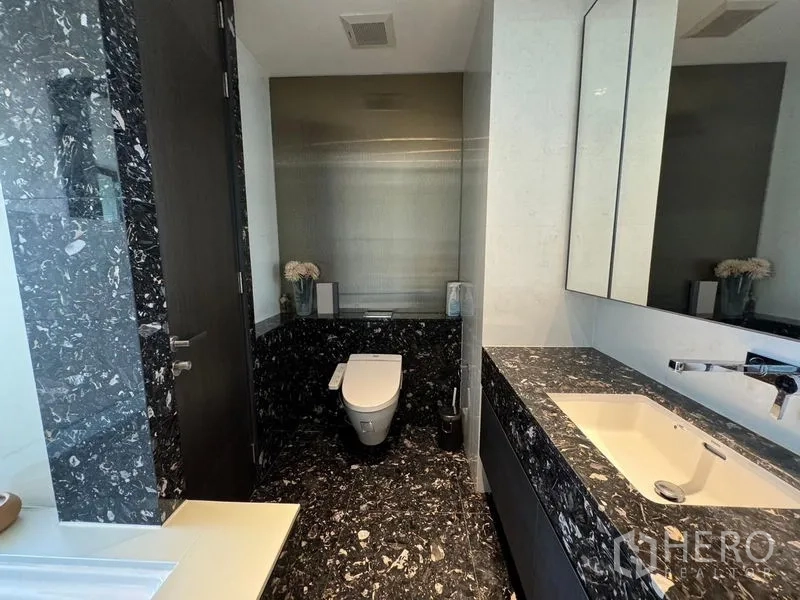Condominium for rent - Guest bathroom with black marble counters, wall-mounted toilet and wide mirror.