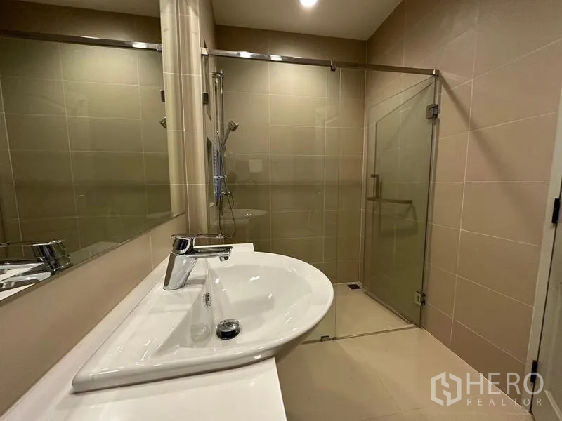 Detached House for rent or sale in Khan Na Yao, Bangkok - Modern bathroom with wide vanity, mirror and glass-enclosed shower.