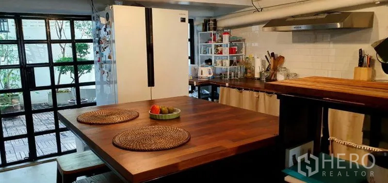 Townhouse for rent in Khlong Toei, Bangkok - Kitchen island with wood top and stools facing patio through black-framed windows.