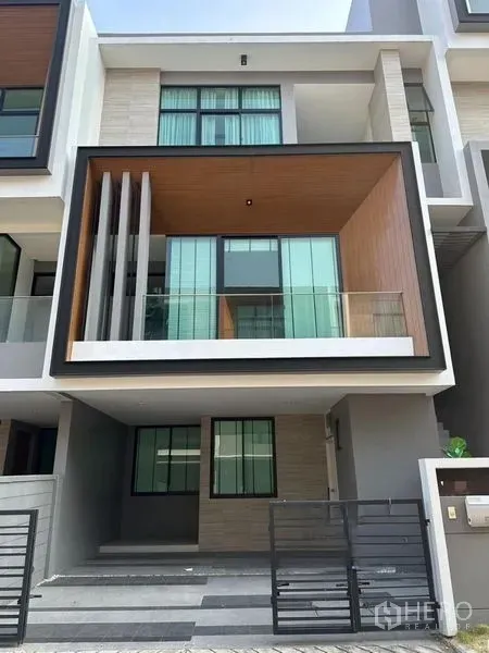Townhouse for sale in Saphan Sung, Bangkok - Modern three-storey townhouse facade with glass balcony, wood accent box, and gated carport.