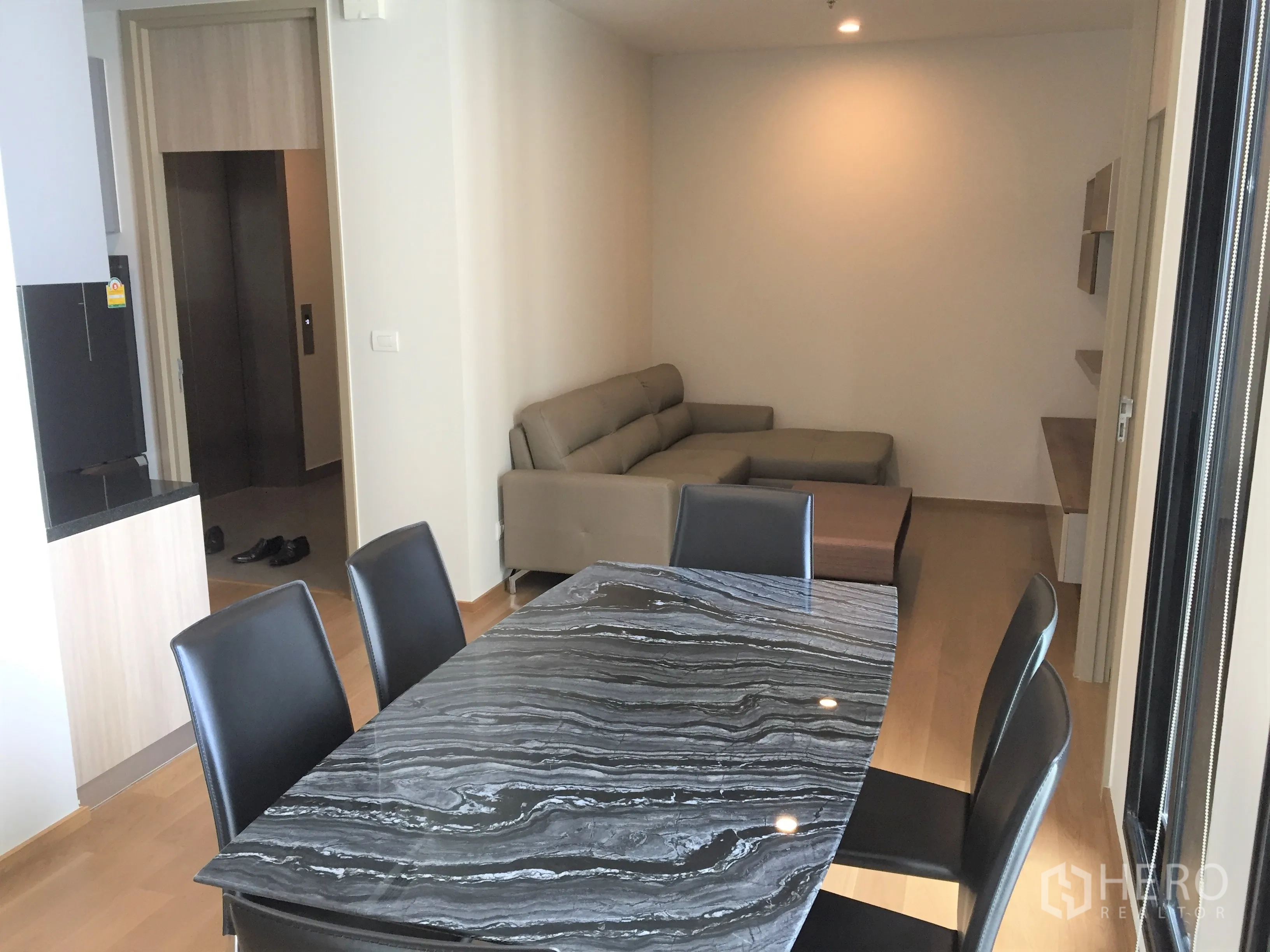 Condominium for rent in Pathum Wan, Bangkok - Open-plan dining and living area with marble-top table, leather sofa and light wood floors.