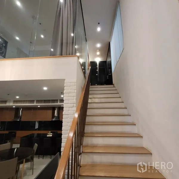 Condominium for rent in Khlong Toei, Bangkok - Wooden staircase with glass railing leading up to a mezzanine level.