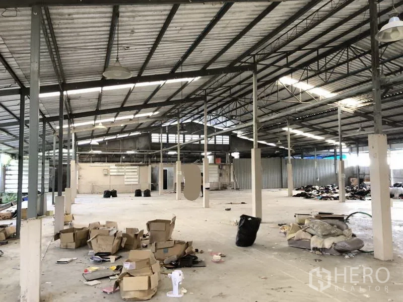 Warehouse for rent or sale in Khlong Luang, Pathum Thani - Wide warehouse bay showing concrete floor, columns, and boxed goods.