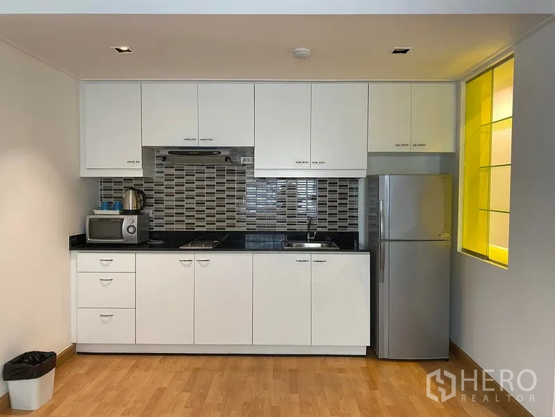 Condominium for rent in Khlong Toei, Bangkok - Modern white kitchenette with tiled backsplash, cooktop, microwave and full-size refrigerator.