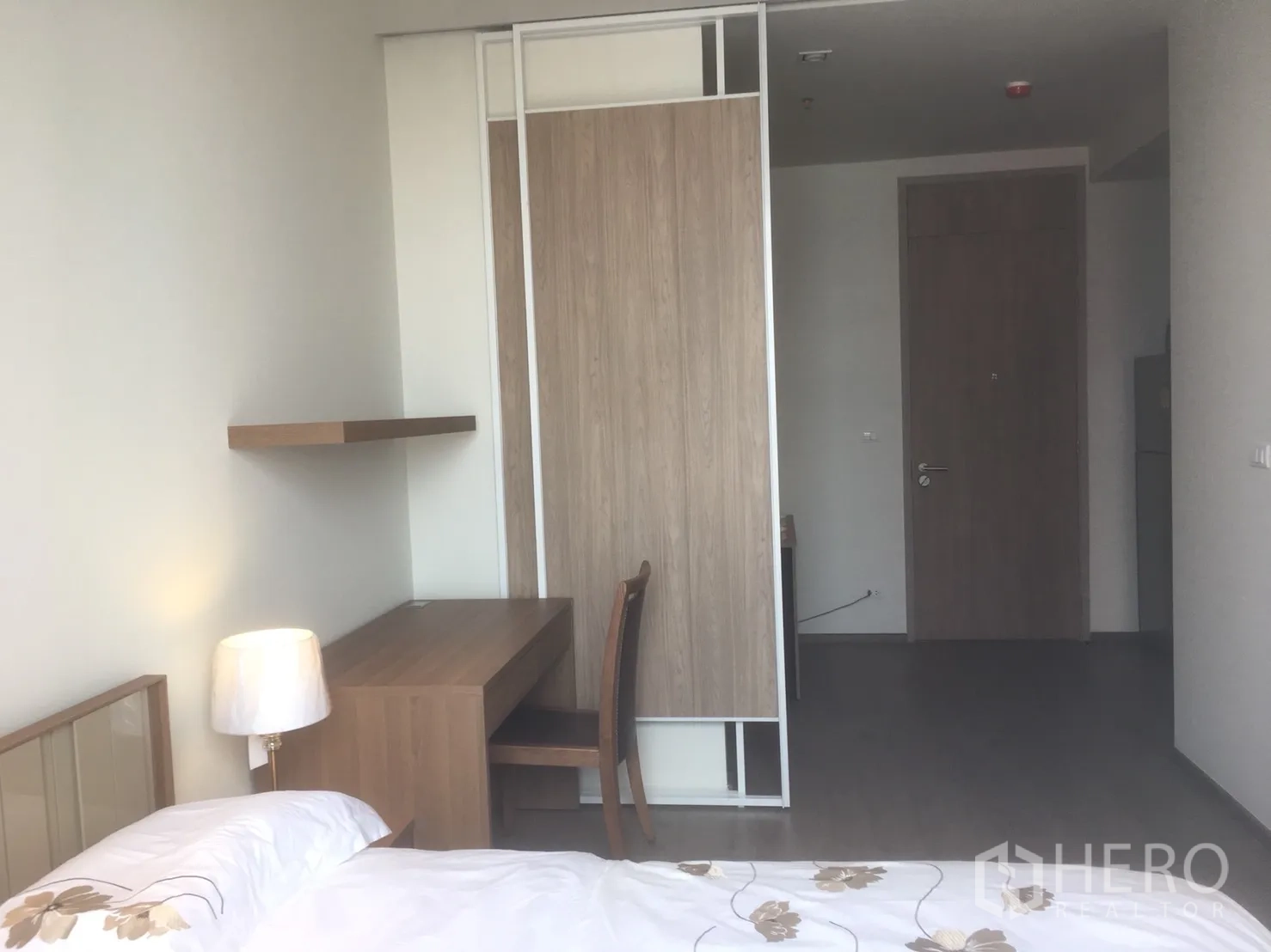Condominium for rent or sale in Khlong Toei, Bangkok - Bedroom workspace with wooden desk, floating shelf and sliding wardrobe doors.