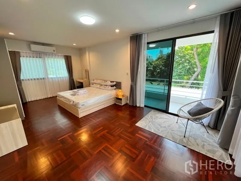 Detached House for rent in Phaya Thai, Bangkok - Spacious bedroom with wood floors, balcony doors and lounge chair.