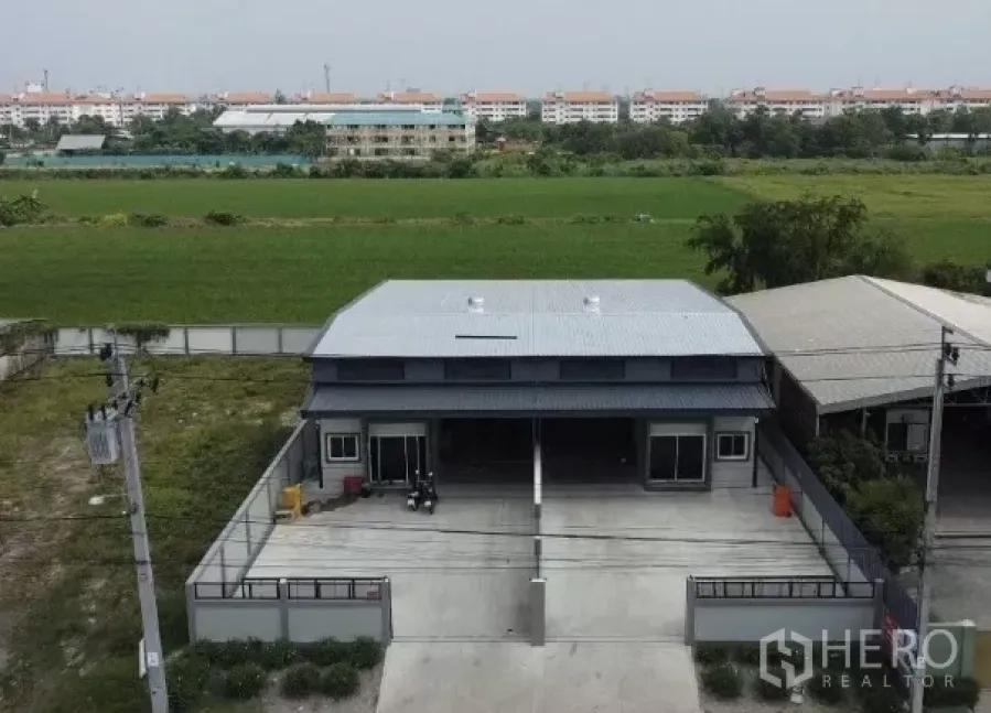 Warehouse for rent in Bang Bua Thong, Nonthaburi - Aerial view of a modern twin-bay warehouse with gated driveway and open fields behind in Bang Bua Thong, Nonthaburi.