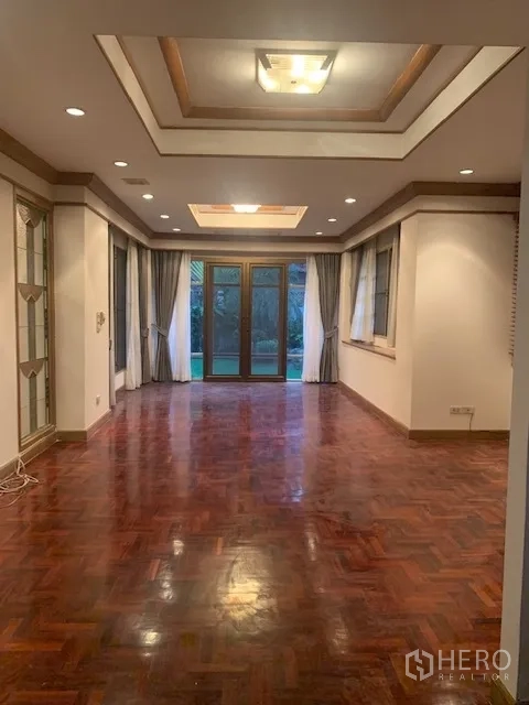 Detached House for rent in Khan Na Yao, Bangkok - Long living room with parquet wood floor, tray ceilings, downlights, and glass doors opening to the garden.