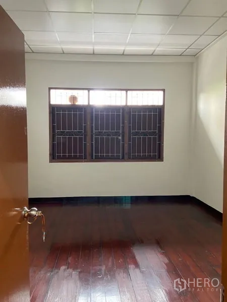 Shophouse for rent in Khlong Toei, Bangkok - Upstairs room with polished wood flooring and windows secured with grilles.