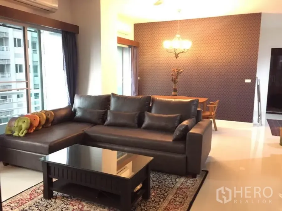 Condominium for rent in Bang Kapi, Bangkok - Bright living room with dark leather sectional, glass coffee table, patterned feature wall and balcony doors in a Bang Kapi condo.