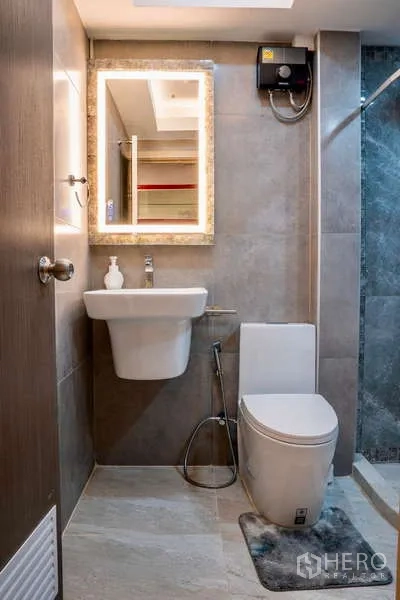 Townhouse for rent in Khlong Toei, Bangkok - Compact bathroom with wall-hung sink, toilet and a backlit vanity mirror.