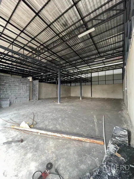 Warehouse for rent in Pathum Thani - Open warehouse interior with high steel truss roof, concrete floor and central columns.