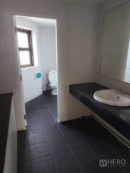 Office Space for rent in Pathum Wan, Bangkok - Modern washroom with large mirror, black floor tiles and a separate toilet room with window.