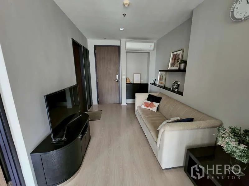 Condominium for sale - Bright living room with TV console, beige sofa, wood flooring, shelves and air conditioning by the entry door.