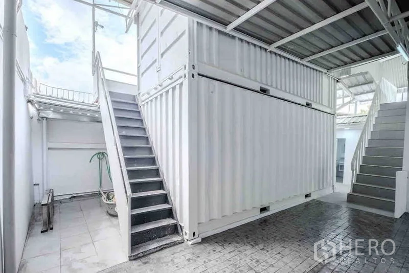 Standalone for rent or sale in Bang Na, Bangkok - Covered outdoor service area featuring stacked white container storage and metal staircases.