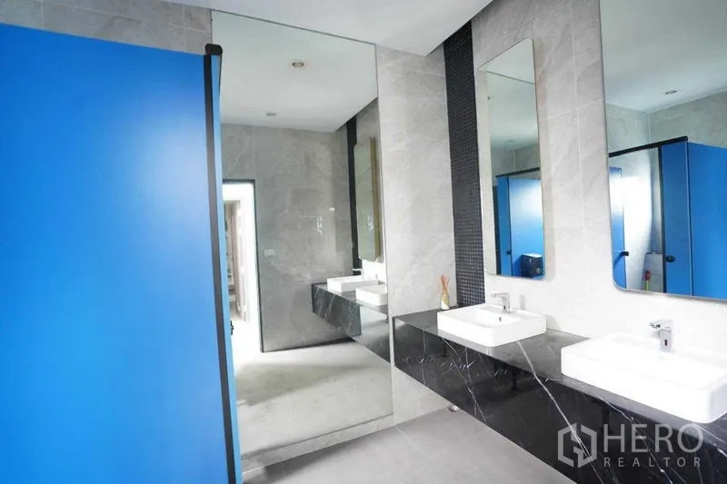 Standalone for rent in Bang Na, Bangkok - Modern restroom with large mirrors, twin sinks and blue partition doors.