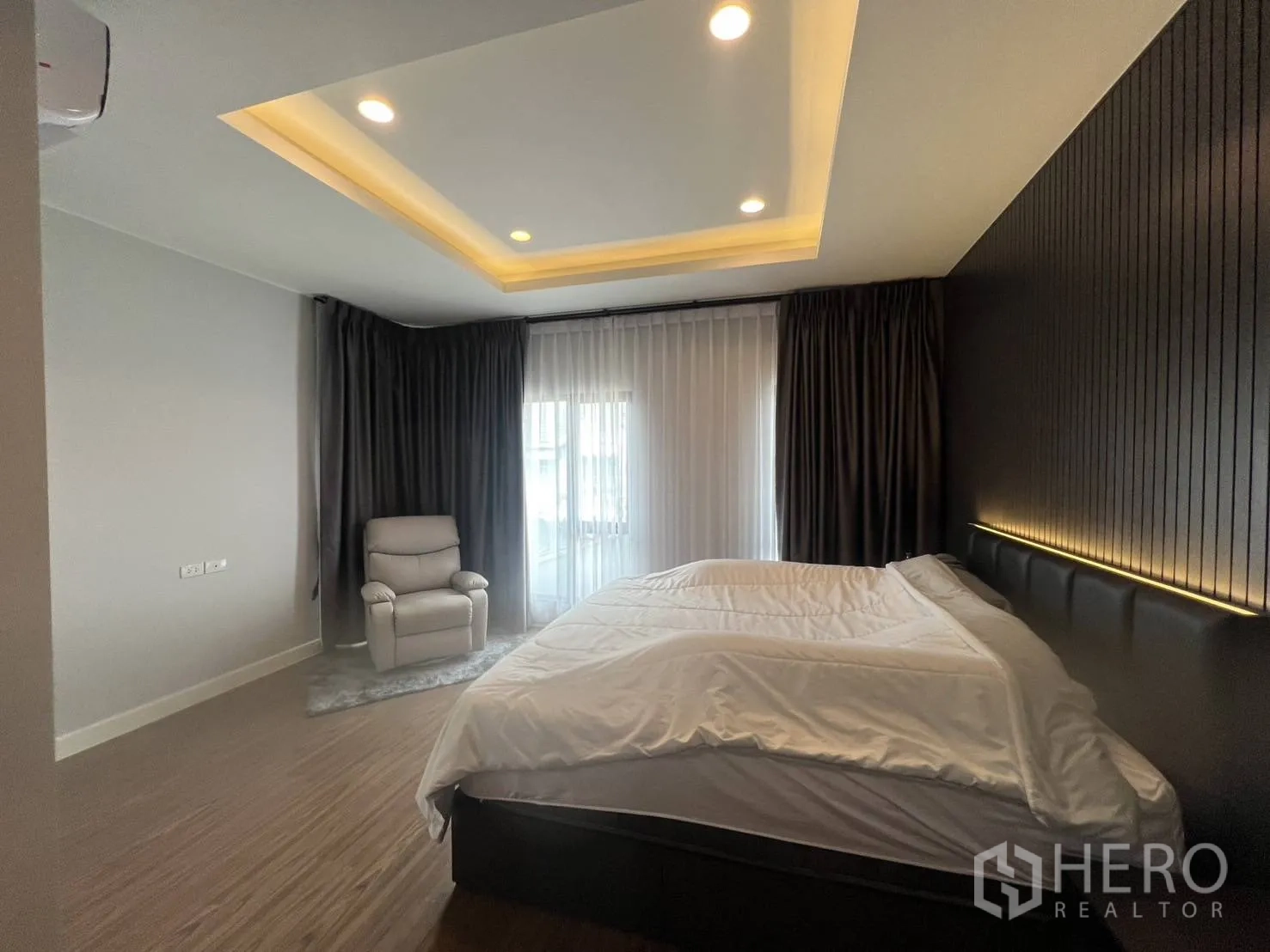 Detached House for rent or sale in Lam Luk Ka, Pathum Thani - Spacious master bedroom with cove lighting, sheer curtains, and an accent wall.