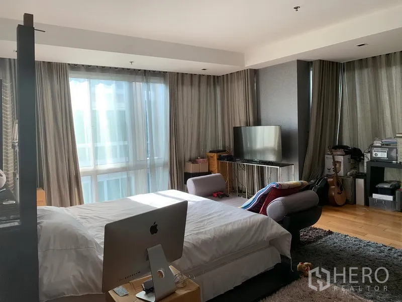 Condominium for sale in Khlong Toei, Bangkok - Bedroom angle showing corner windows, sofa seating and a TV console.