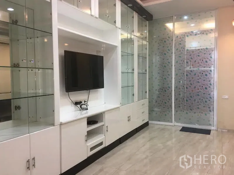 Townhouse for rent in Bang Rak, Bangkok - Built-in white TV cabinet with glass display shelves, wall-mounted screen and sliding frosted doors.