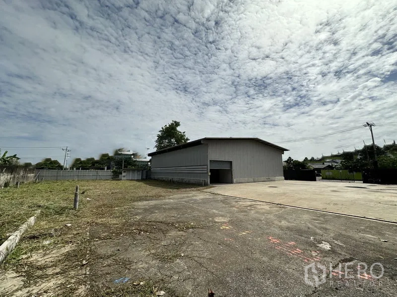 Warehouse for rent in Min Buri, Bangkok - Side angle of the warehouse showing an expansive yard and boundary wall for truck maneuvering.