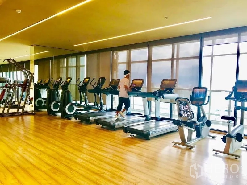 Condominium for rent in Khlong Toei, Bangkok - Fitness center with rows of treadmills and cardio machines facing floor-to-ceiling windows.