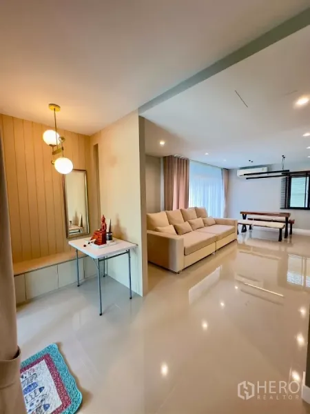 Detached House for rent in Samut Prakan - Open-plan living and dining area with large beige sofa, pendant lights and glossy floors.