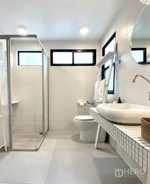 Townhouse for rent in Khlong Toei, Bangkok - Bright bathroom with shower stall, long vanity counter and white wall tiles.