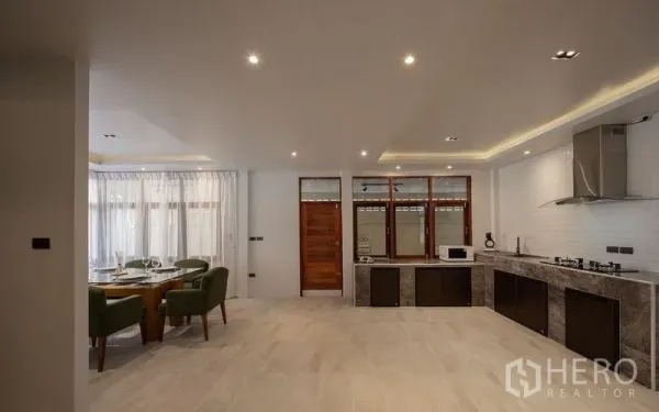 Detached House for sale in Chatuchak, Bangkok - Open-plan kitchen with long countertop, gas hobs, hood and recessed lighting beside the dining area.