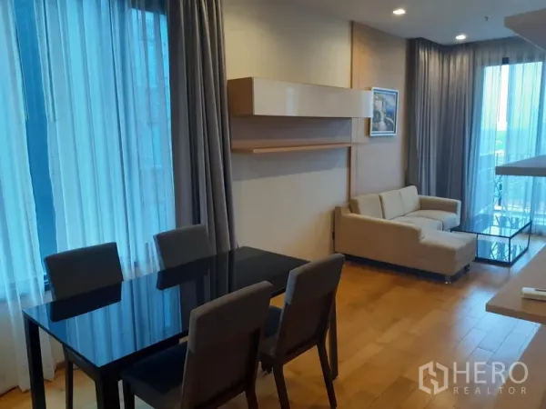 Condominium for rent in Khlong Toei, Bangkok - Open-plan living and dining room with sofa, glass coffee table and balcony access via sliding doors.