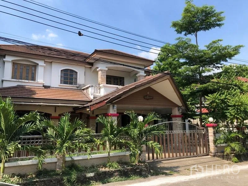 บ้าน ขายในPak Kret, Nonthaburi - บ้านเดี่ยว 2 ชั้น ปากเกร็ด นนทบุรี หลังคากระเบื้อง ระเบียง หน้าบ้านมีรั้วเหล็กและสวนปาล์ม ใต้ท้องฟ้าโปร่ง