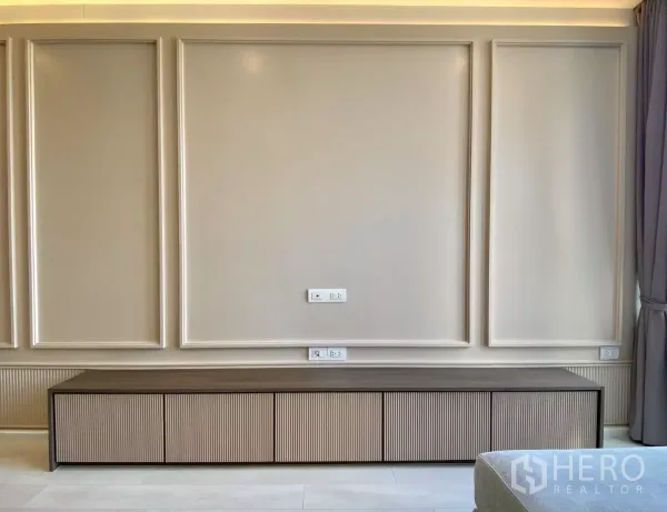 Condominium for sale in Pathum Wan, Bangkok - Feature TV wall with elegant paneling and long low storage console with power outlets.