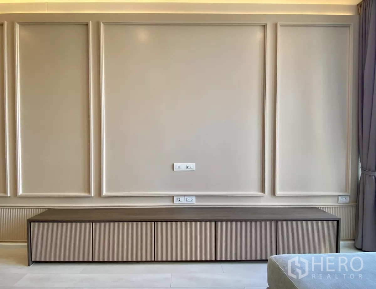 Condominium for sale in Pathum Wan, Bangkok - Feature TV wall with elegant paneling and long low storage console with power outlets.