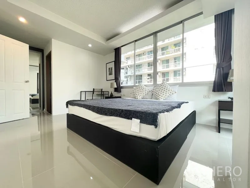 Condominium for rent in Khlong Toei, Bangkok - Spacious bedroom with big windows and bedside tables facing nearby block.