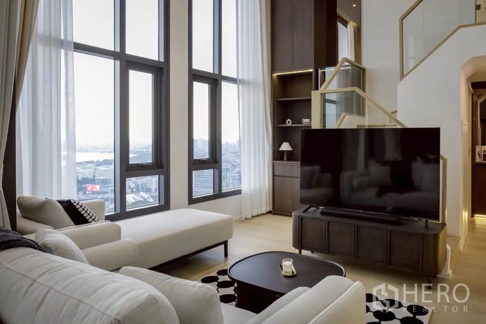 Condominium for rent in Khlong Toei, Bangkok - Lounge with chaise sofa facing large TV, framed by towering windows.