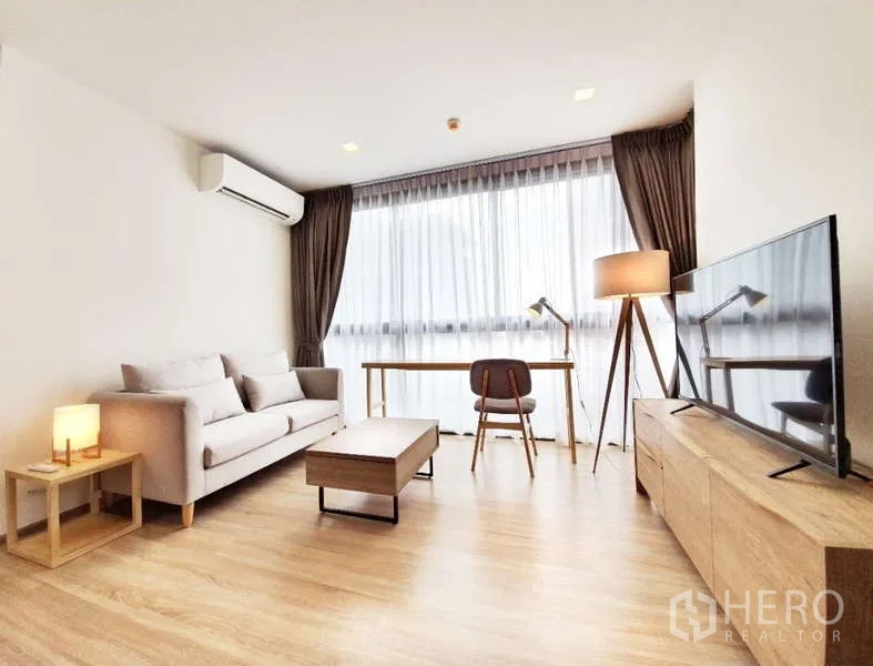 Condominium for sale in Watthana, Bangkok - Bright living room with sofa, TV console, wooden floors and floor-to-ceiling windows in an Ekkamai condo.
